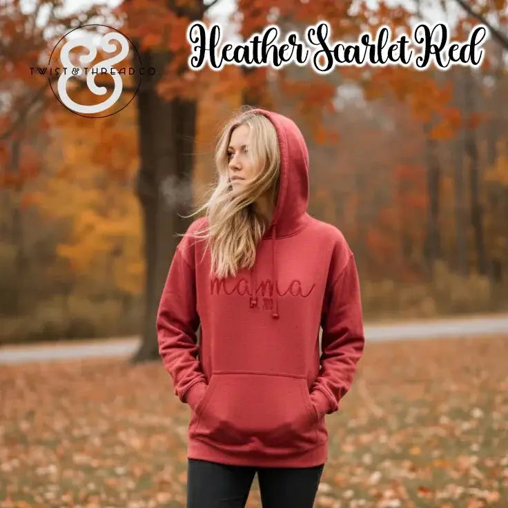 Woman wearing heather scarlet red hoodie with mamas emblem in autumn park with colorful fall leaves