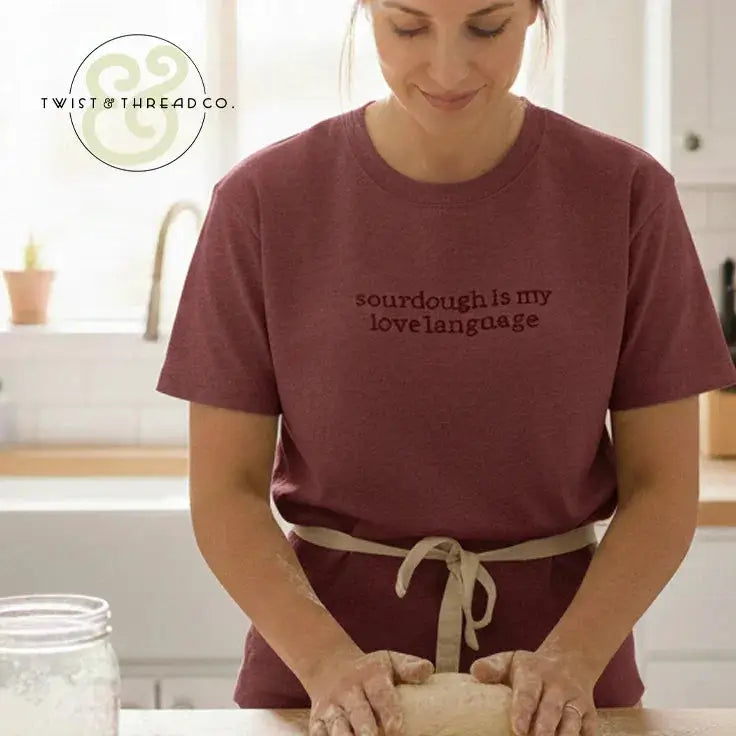 Woman wearing a maroon shirt with "sourdough is my love language" kneading dough in a bright kitchen