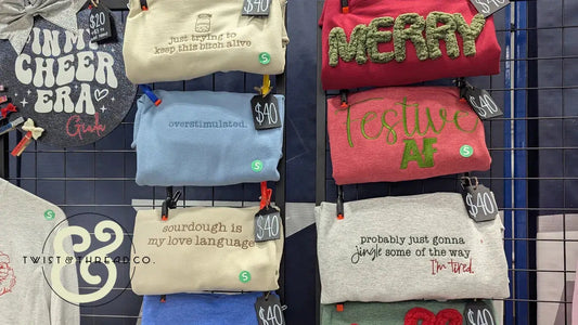 Display of colorful, embroidered sweatshirts with witty sayings at Twist & Thread Co. booth