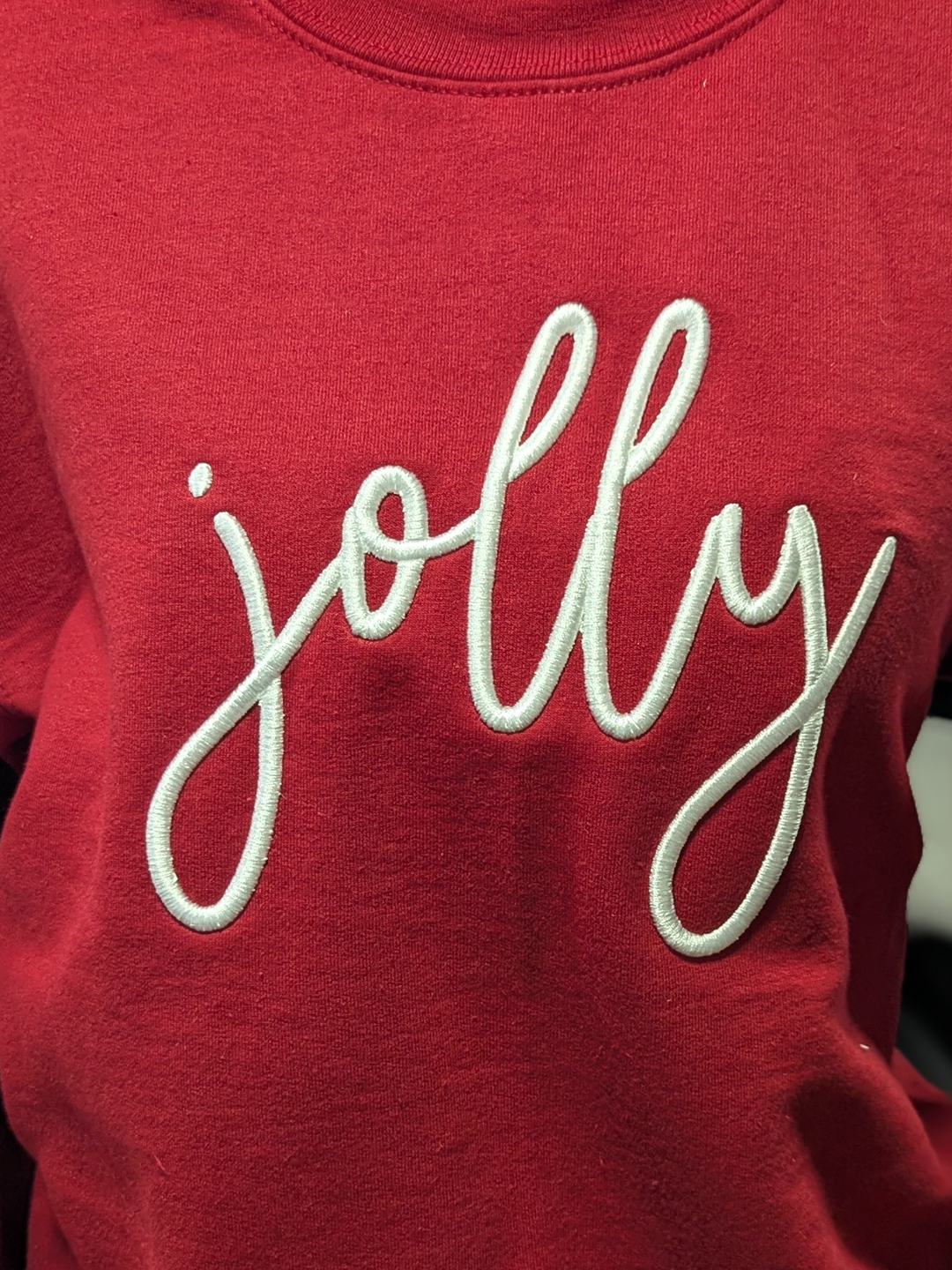 Smiling woman wearing red hoodie with 'jolly' text in front of decorated Christmas tree with lights and ornaments