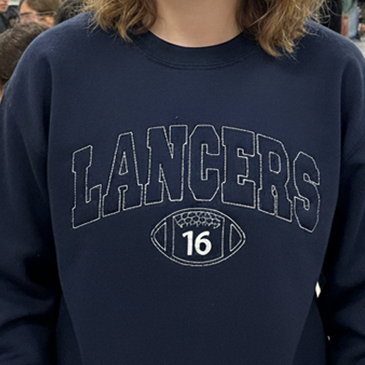 Young woman in pink 'Cheer' crewneck shouting at nighttime football stadium crowd