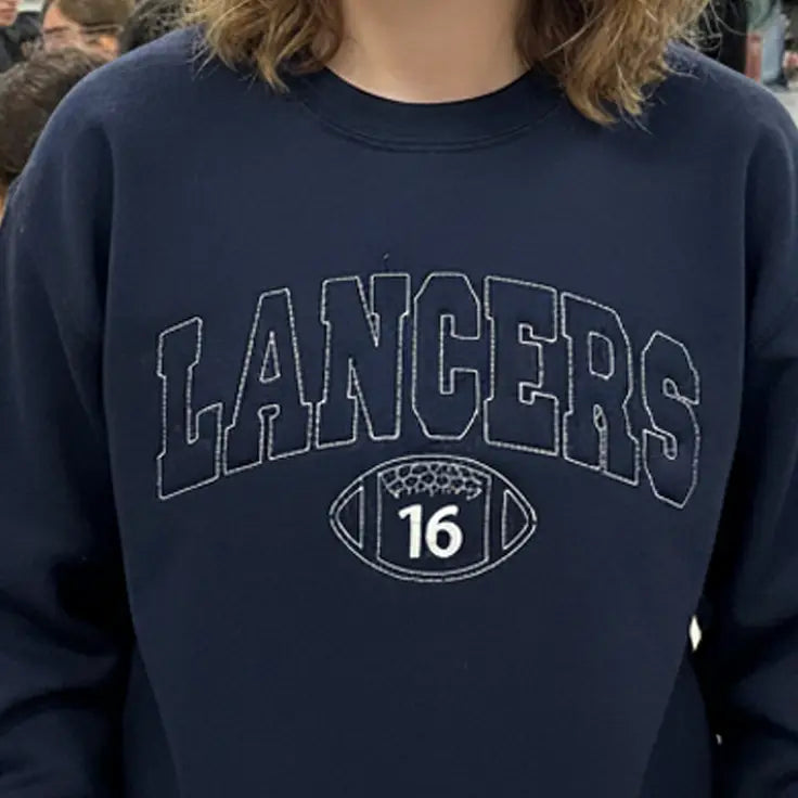 Young woman in pink 'Cheer' crewneck shouting at nighttime football stadium crowd