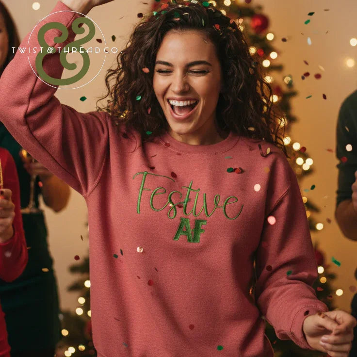 Smiling woman wearing pink Festive AF sweatshirt celebrating with confetti at Christmas party