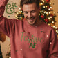 Smiling man wearing a red sweater with green text 'Festive AF' in front of a decorated Christmas tree