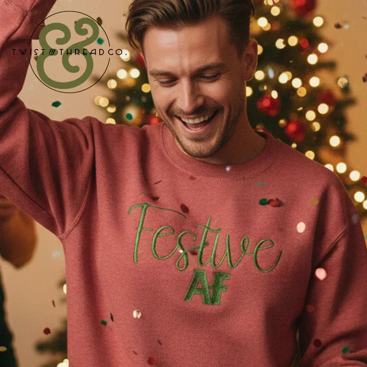 Smiling man wearing a red sweater with green text 'Festive AF' in front of a decorated Christmas tree