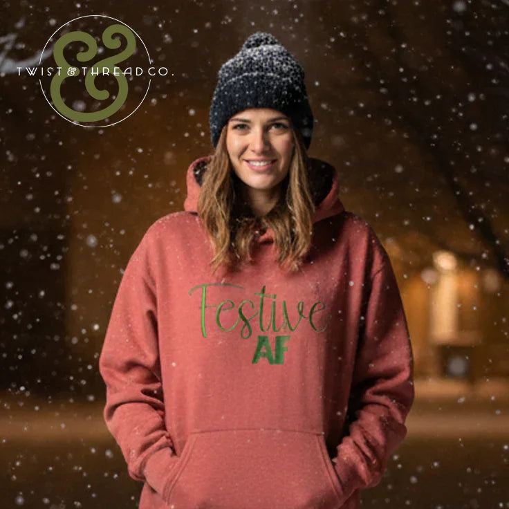Smiling woman wearing a pink Festive AF hoodie and black beanie in a snowy outdoor setting