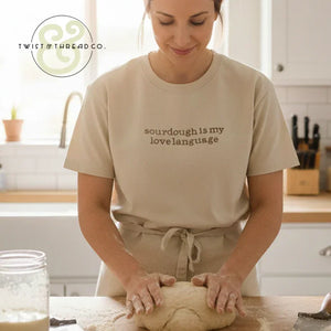 Woman kneading sourdough bread dough in bright kitchen, wearing shirt that says sourdough is my love language