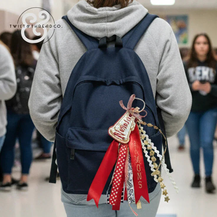 Navy backpack with custom red ribbon bag tag in school hallway, student wearing gray hoodie