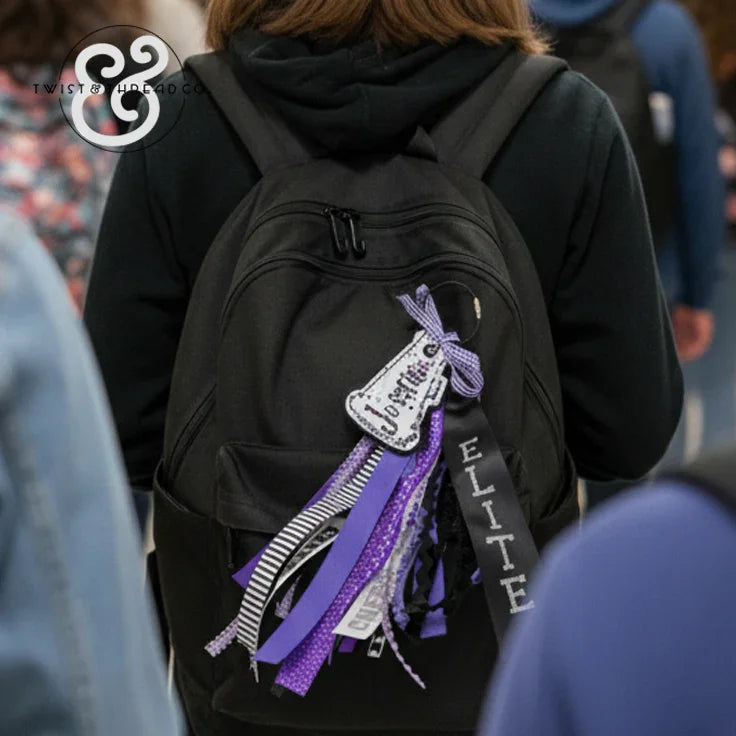 Black backpack with custom purple and black bag tag, ribbons, and 'Elite' lettering at school