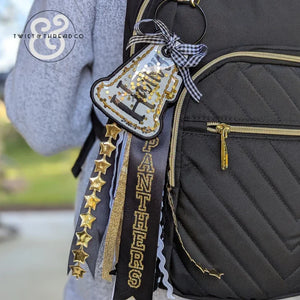Black backpack with gold and black 'PANTHERS' bag tag featuring stars and ribbon accents