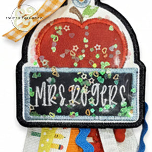 Teacher bag tag with embroidered red apple and chalkboard label reading 'Mrs Rogers' with decorative confetti