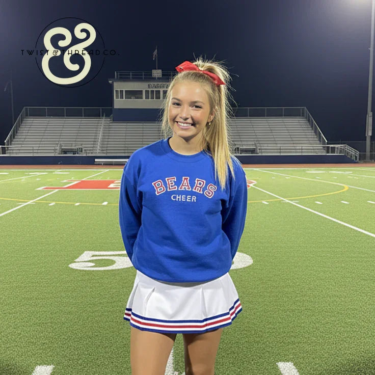 Smiling cheerleader in blue Bears Cheer sweatshirt and skirt on football field, Twist & Thread Co. apparel