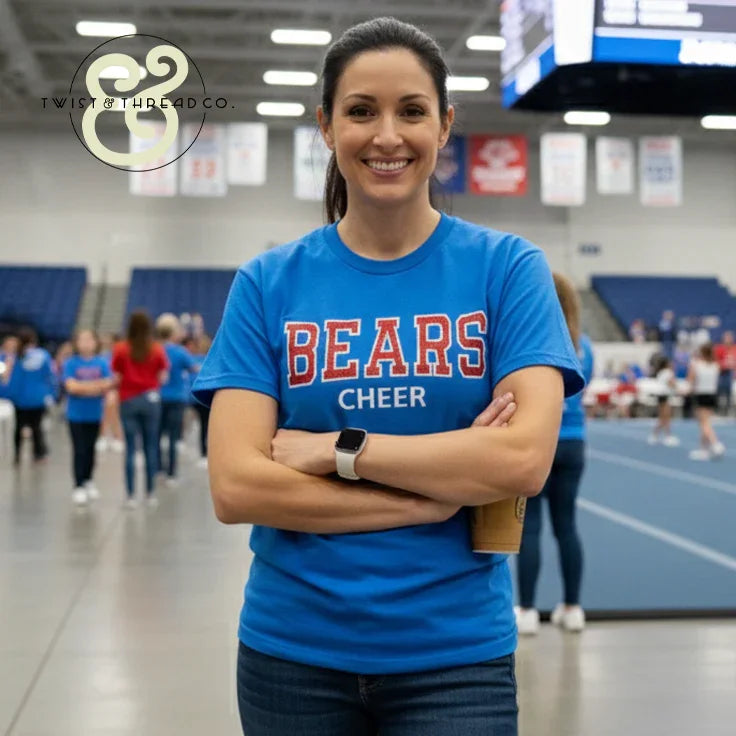 Smiling woman in blue BEARS CHEER embroidered shirt at indoor sports event, Twist & Thread Co.