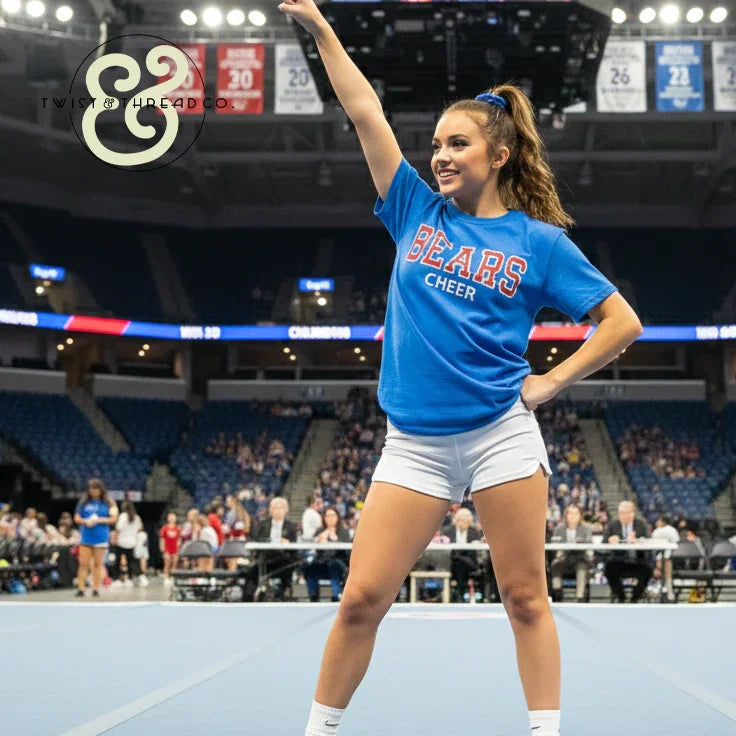 Cheerleader in blue BEARS CHEER shirt performing at indoor arena, Twist & Thread Co. apparel