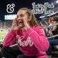 Girl in safety pink 'Cheer' sweatshirt cheering at stadium, crowd and field in background