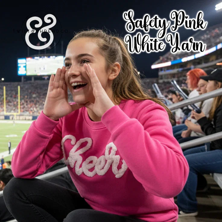 Girl in safety pink 'Cheer' sweatshirt cheering at stadium, crowd and field in background