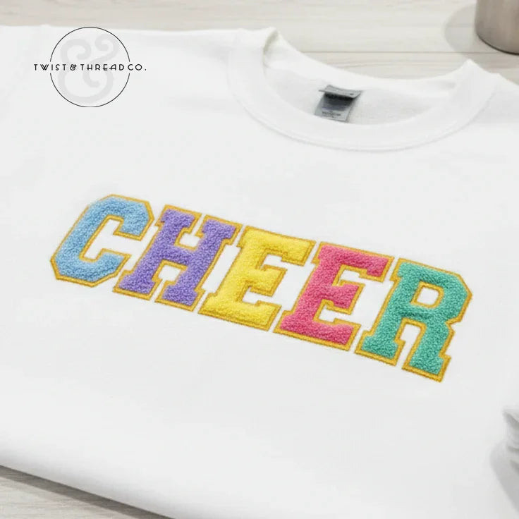 White sweatshirt with colorful chenille CHEER letters, Twist & Thread Co. branding, flat lay