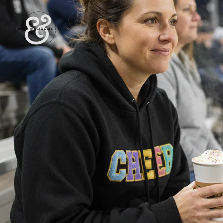 Woman in black CHEER hoodie holding a coffee with sprinkles at indoor bleachers