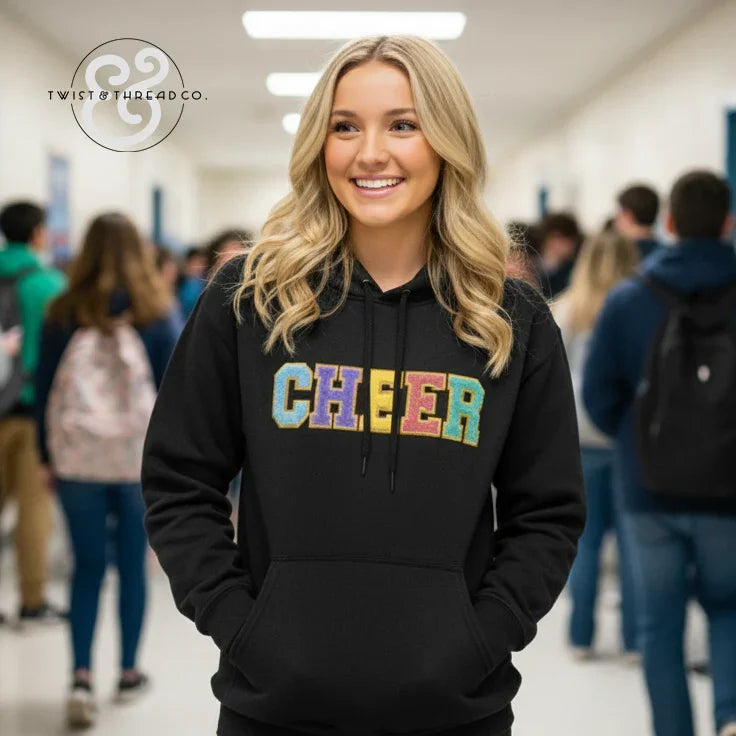 Smiling woman in school hallway wearing black hoodie with colorful CHEER text