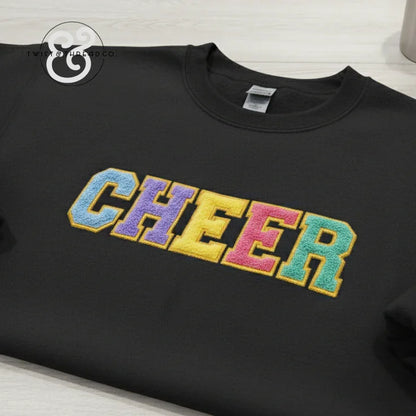 Black sweatshirt with colorful embroidered CHEER letters, cheerleading apparel flat lay