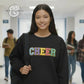 Smiling student in black CHEER sweatshirt walking in school hallway with backpack.