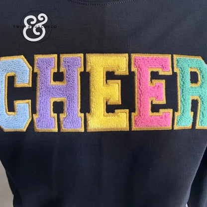 Close-up of colorful chenille embroidered letters spelling CHEER on black fabric