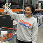 Smiling woman in a custom embroidered Costco-themed sweatshirt shopping in a warehouse.