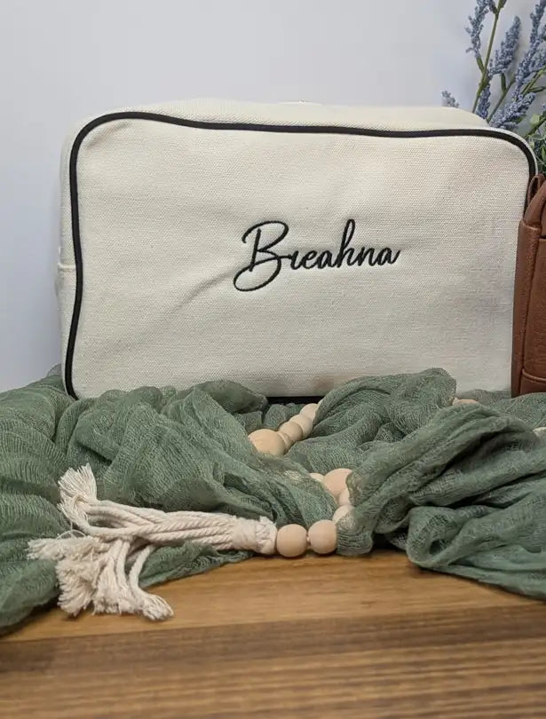 Cream-colored canvas化妆包 with black embroidered name ’breaahna’ and a contrasting black trim.