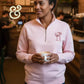 Woman wearing light pink embroidered quarter-zip sweatshirt with cupid cocktail design, holding coffee at Twist & Thread Co. cafe.