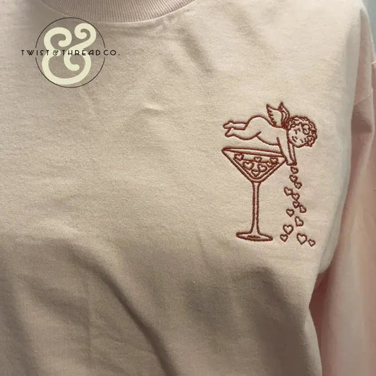 Embroidered pink shirt with cupid pouring hearts into a cocktail glass by Twist & Thread Co.