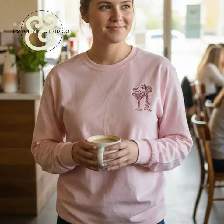 Woman in pink embroidered sweatshirt from Twist & Thread Co. holding coffee in a cafe