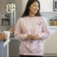 Woman in pink embroidered sweatshirt by Twist & Thread Co. smiling in modern kitchen