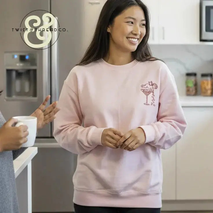 Woman in pink embroidered sweatshirt by Twist & Thread Co. smiling in modern kitchen