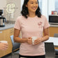 Woman in office wearing Twist & Thread Co. pink embroidered Cupid t-shirt, holding a mug