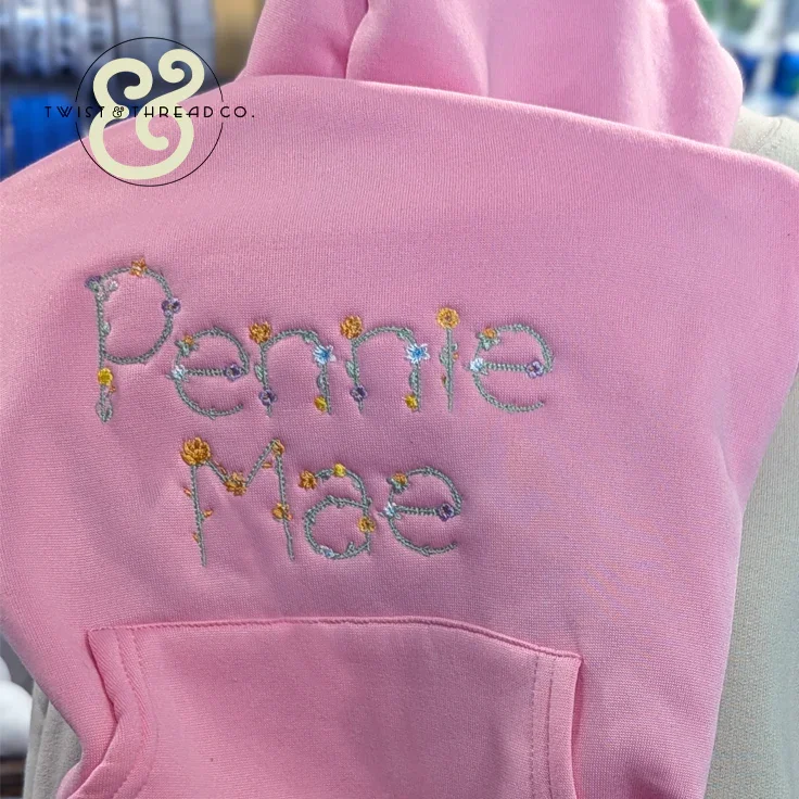 Pink dog hoodie with embroidered name Penny Mae featuring colorful floral stitch accents from Twist & Thread Co.
