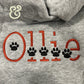 Gray hoodie with custom embroidered name 'Ollie' in orange and black paw prints at Twist & Thread Co.