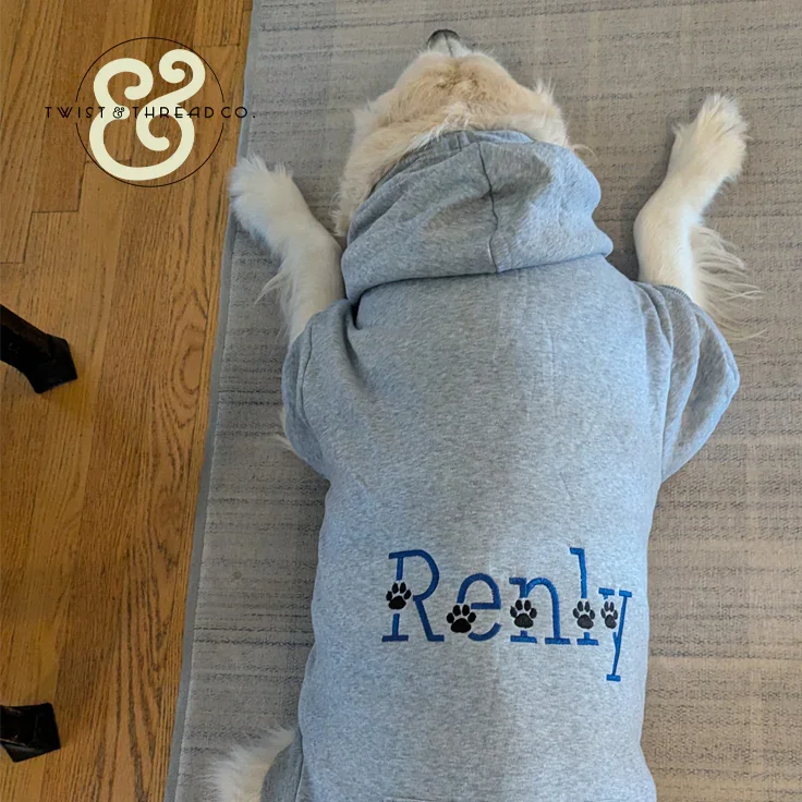 Golden retriever dog wearing custom gray hoodie embroidered with name Renly and paw prints, lying on rug and hardwood floor