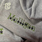 Close-up of gray hoodie with custom green embroidery spelling 'Malligan' featuring black paw prints, from Twist & Thread Co.