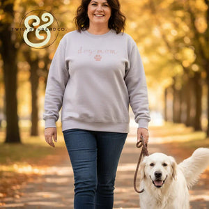 Woman in a 'dog mom' custom embroidered sweatshirt walking a golden retriever outdoors in autumn