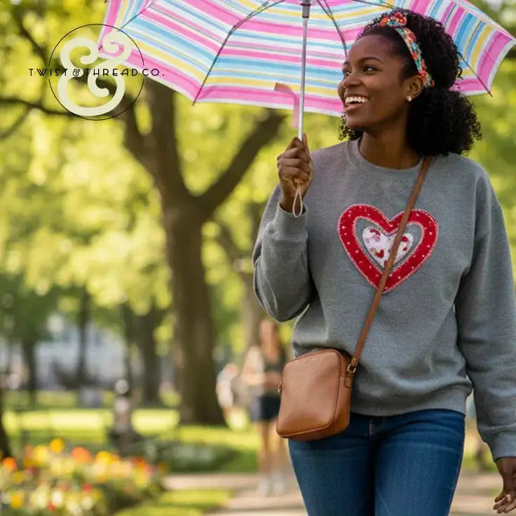 Woman wearing Twist & Thread Co. embroidered heart sweatshirt, holding striped umbrella outdoors
