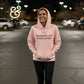 Pink hoodie with text dumbbells over dumb people worn by smiling woman in parking lot at night