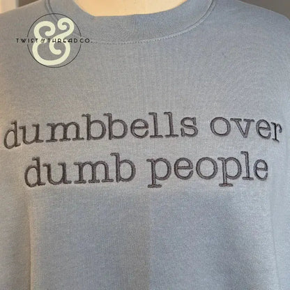 Light blue shirt with text embroidered saying dumbbells over dumb people fitness quote