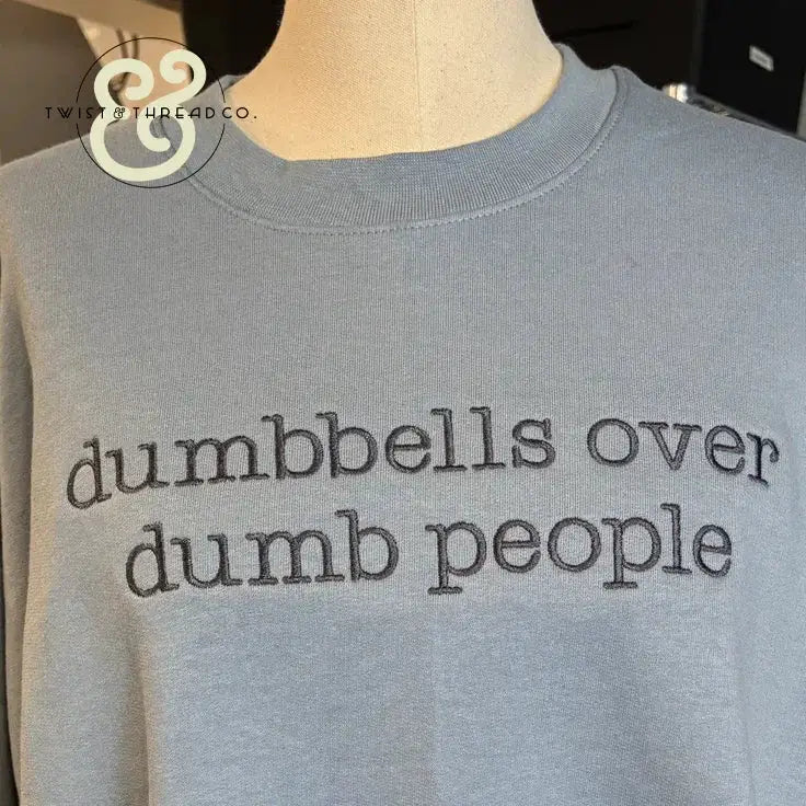 Light blue shirt with embroidered text saying dumbbells over dumb people fitness slogan