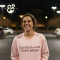 smiling woman wearing light pink sweatshirt with dumbbells over dumb people text, night outdoor setting