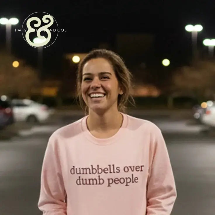 smiling woman wearing light pink sweatshirt with dumbbells over dumb people text, night outdoor setting