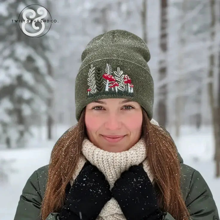 Woman in snowy forest wearing green embroidered winter hat with red mushrooms