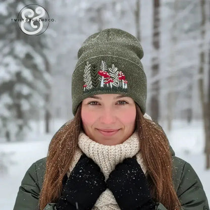 Woman in snowy forest wearing green embroidered winter hat with red mushrooms