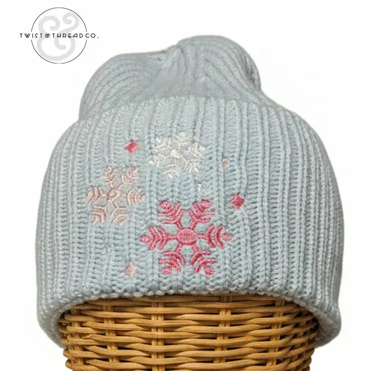 Light blue knit winter hat with pink and white snowflake embroidery on a wicker stand