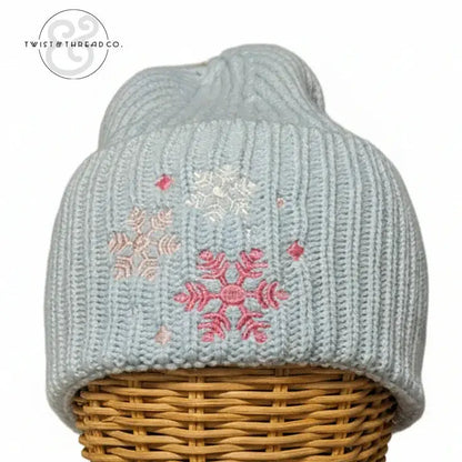 Light blue knit winter hat with pink and white snowflake embroidery on a wicker stand