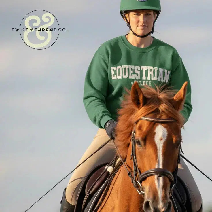 Equestrian athlete in green helmet and sweatshirt riding chestnut horse with white blaze, outdoor setting